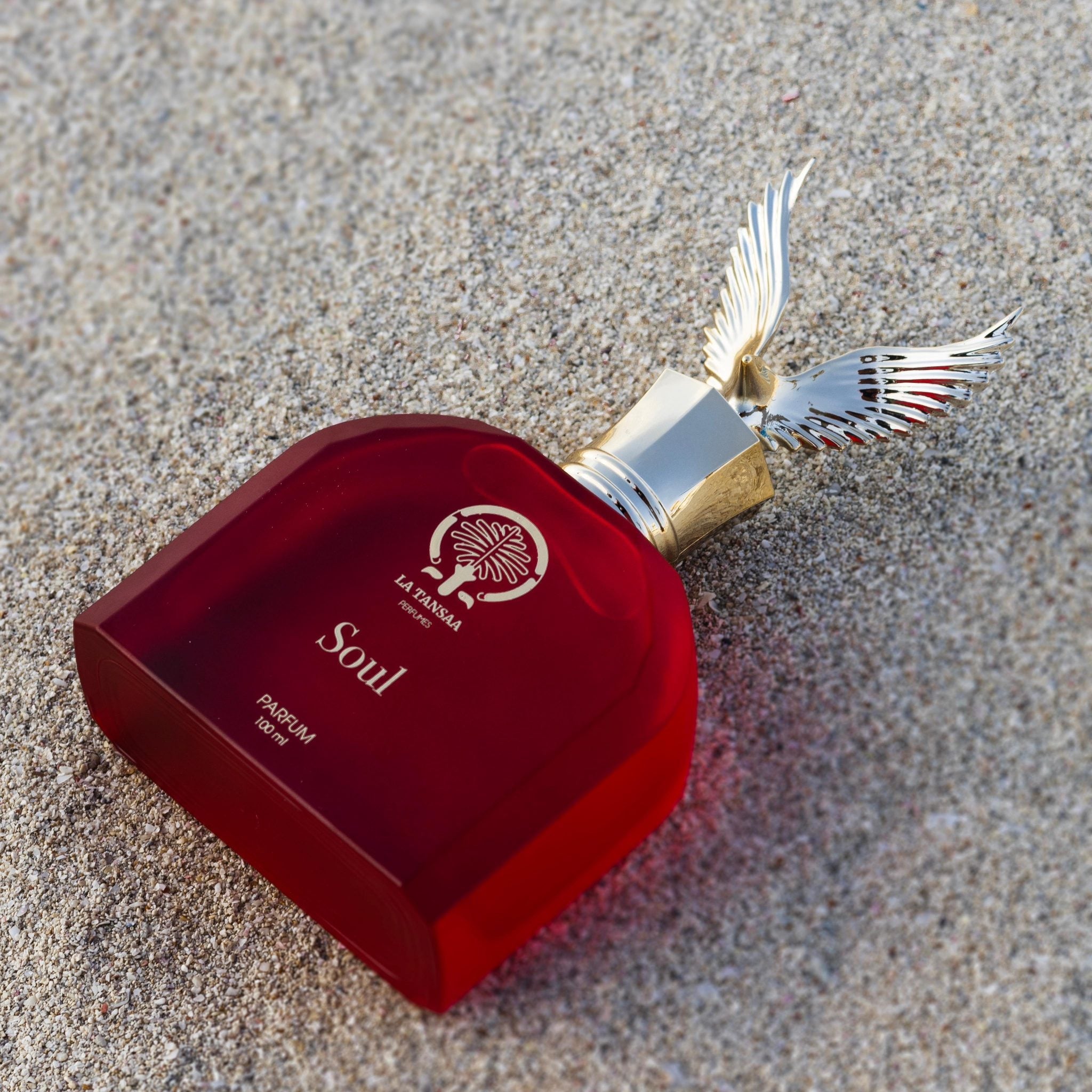 Red perfume bottle with silver cap and wings on a sandy surface